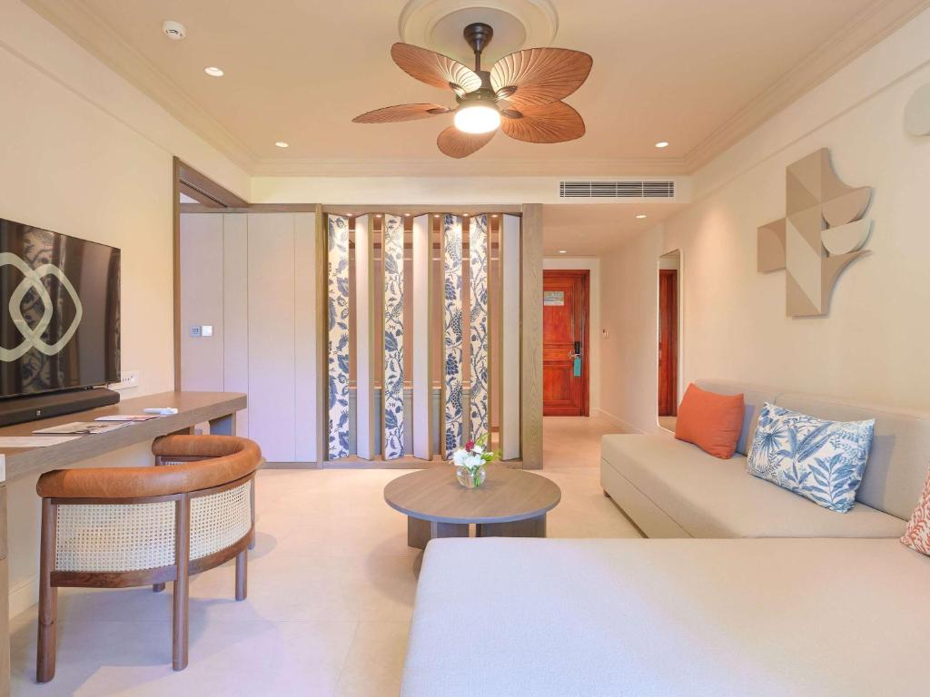 Mūsdienīga viesnīcas numura iekārtojums ar komfortablu dīvānu, koka krēsliem un televizoru, kas rada relaksējošu atmosfēru. Interjers ir gaišs un elegants, ar dekoratīvām detaļām un modernām apgaismojuma iespējām.