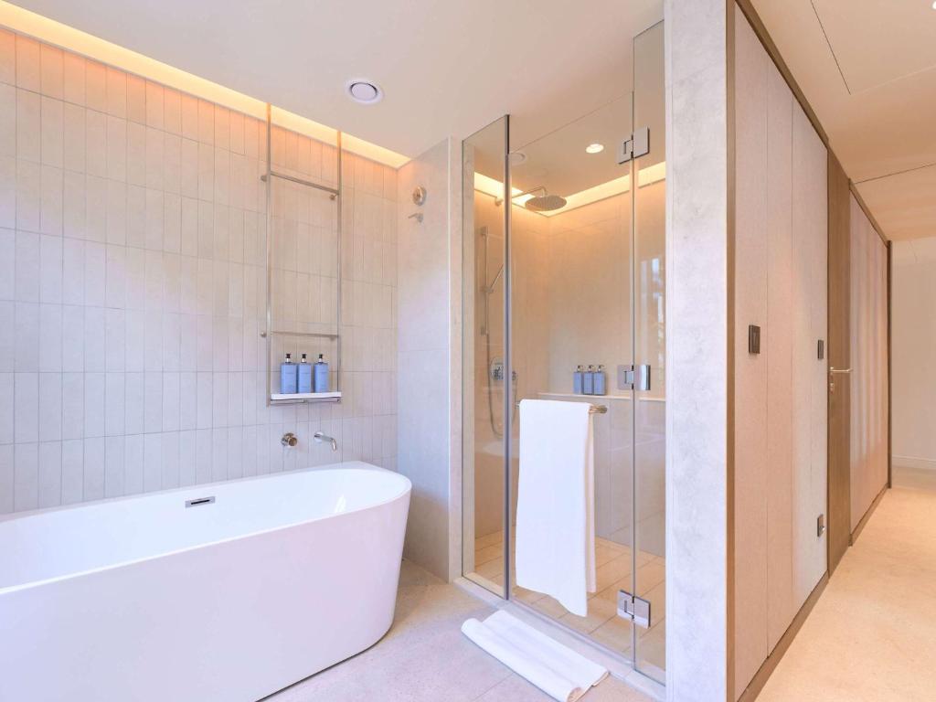 Mūsdienīgs vannas istabas interjers ar brīvo stūra vannu un caurspīdīgu dušas kabīni, papildināts ar minimālistisku dizainu un siltu apgaismojumu.