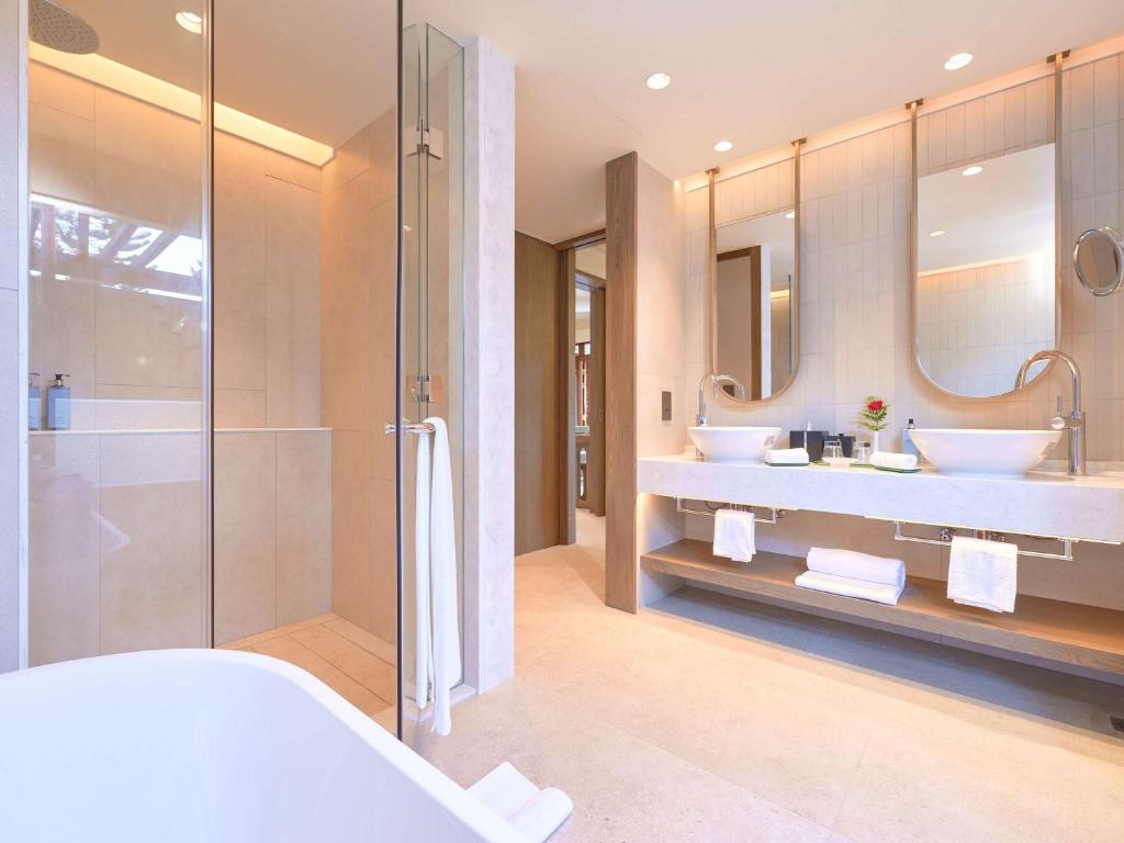 Mūsdienīgs vannas istabas interjers ar stikla dušu, diviem izlietnēm un elegantiem spoguļiem. Telpa ir gaiša un plaša, ar minimālistisku dizainu un dabīgām krāsām.