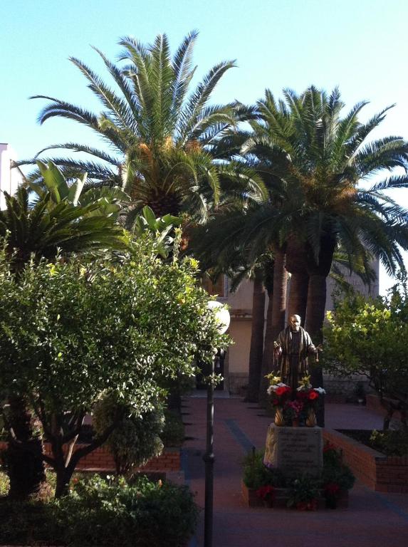 Vietā ar palmām un zālēm redzams piemineklis, kas rotāts ar ziediem. Skats uz skaidru debesu fonu veido mierīgu un patīkamu atmosfēru.