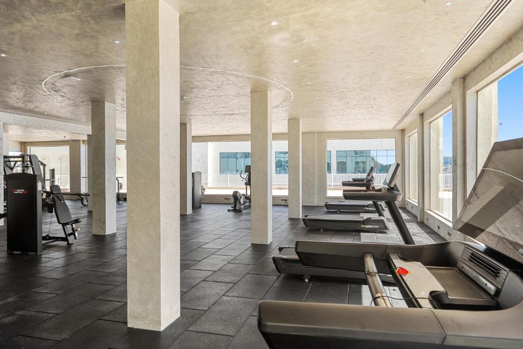 Mūsdienīgs trenažieru zāles interjers ar skatu uz ārpusi, kas aprīkota ar modernām fitnesa ierīcēm un plašiem logiem, kas nodrošina dabīgu apgaismojumu.