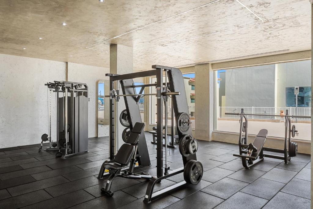 Mūsdienīgs sporta zāles interjers ar dažādām treniņu iekārtām un plašiem logiem, kas nodrošina dabīgu apgaismojumu. Ideāls vieta aktīvām nodarbēm un fitnesa treniņiem.