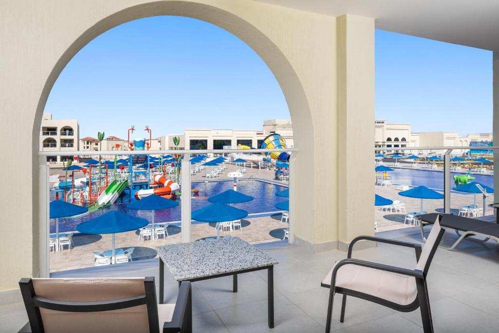 Skats no terases uz ūdens atrakciju parku ar baseinu un saules ēnām. Krāsaini slidkalniņi un pludmales krēsli veido jautru un relaksējošu atmosfēru.