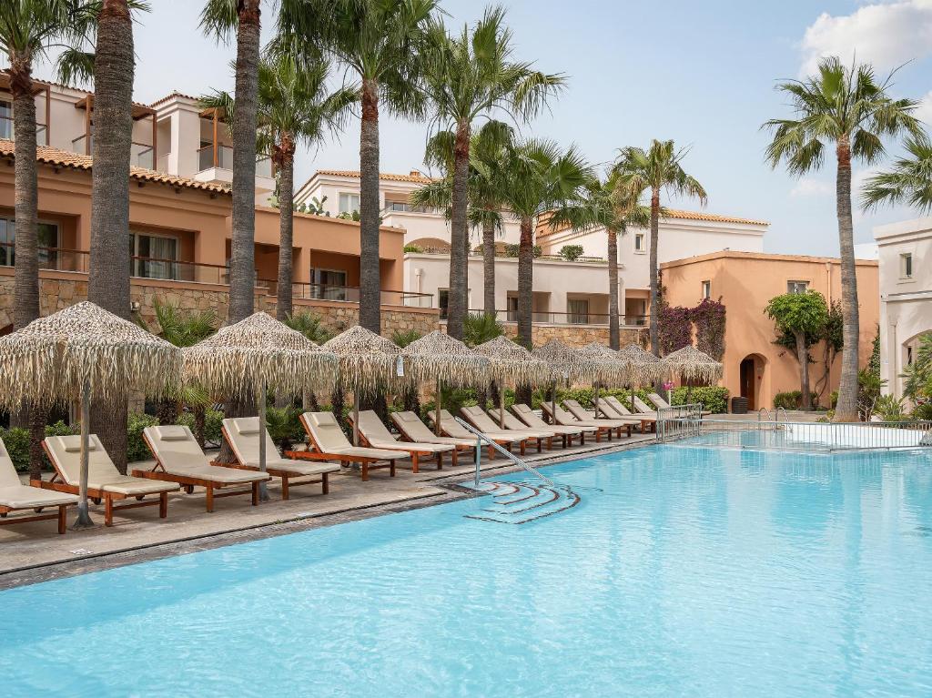 Grecotel Marine Palace & Aqua Park peldbaseins ar palmām un sauļošanās krēsliem