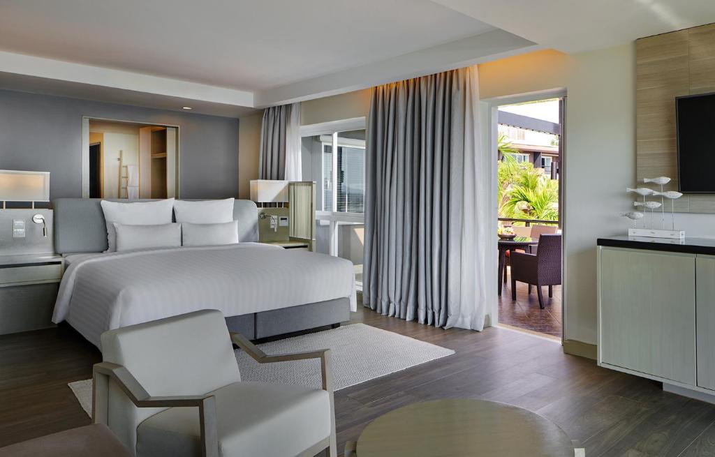 Mūsdienīga viesnīcas numura interjers ar lielu gultu, sēdvietām un terasi, kas sniedzas uz dārzu. Gaisma plūst caur plašajiem logiem, radot patīkamu atmosfēru.