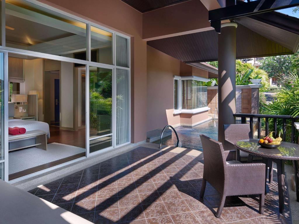 Labi iekārtota terase ar galdu un krēsliem, kas izskatās uz skaistu dārzu. Logi atveras uz modernu guļamistabu, radot mierīgu un relaksējošu atmosfēru.