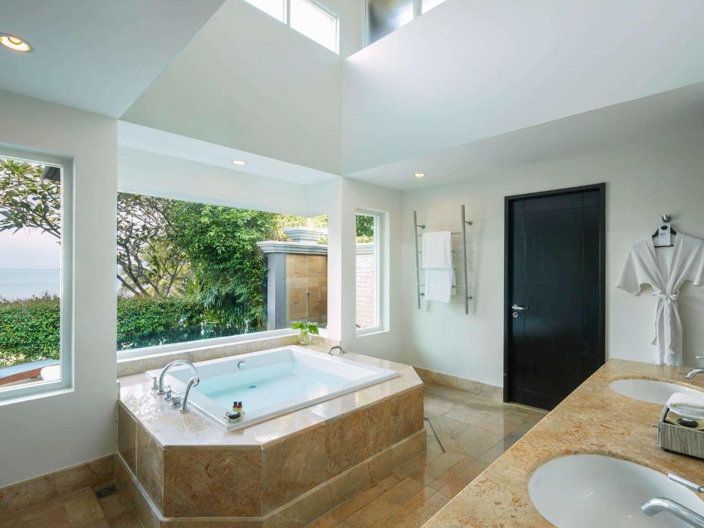 Mūsdienīgs un gaišs vannas istabas interjers ar koka akcentiem, kas ietver burbuļvannu un lielus logus, kas piedāvā skatu uz dabu.