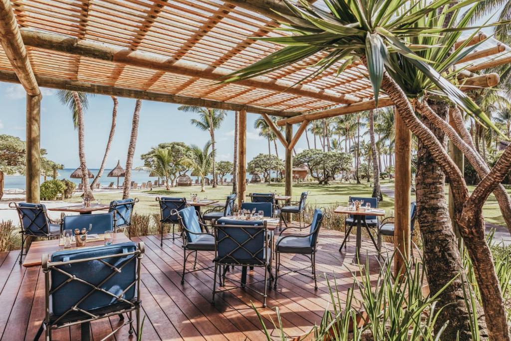 Restorāna terase ar elegantiem zila krāsas krēsliem un galdiem, kas atrodas pie pludmales, ar palmām un dārzu fonā. Ideāla vieta relaksācijai un baudīšanai.