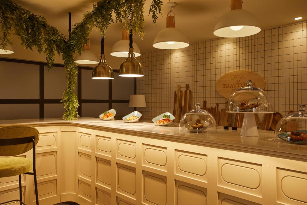Mūsdienīgs restorāns ar elegantu bāra zonu, kas rotāta ar zaļumiem un izsmalcinātu apgaismojumu. Uz letes izvietoti dažādi ēdieni, kas pasniegti zem glāzēm.
