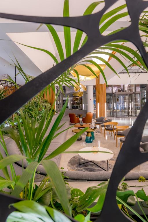 Mūsdienīgs viesnīcas interjers ar zaļām augu kompozīcijām un elegantiem sēdvietām. Gaismas elementi rada siltu atmosfēru.