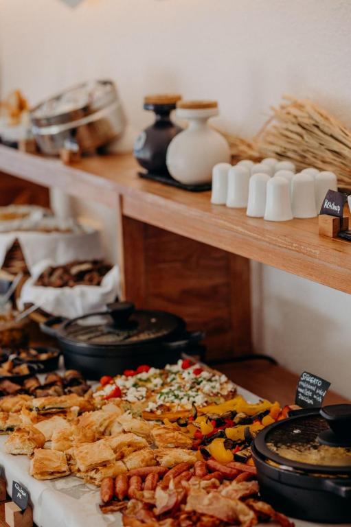 Bagātīgs bufetes galds ar dažādām uzkodām, ieskaitot maizes izstrādājumus, gaļas produktus un dārzeņus, kā arī garšvielas un mērces. Galds rotāts ar elegantu koka plauktu.