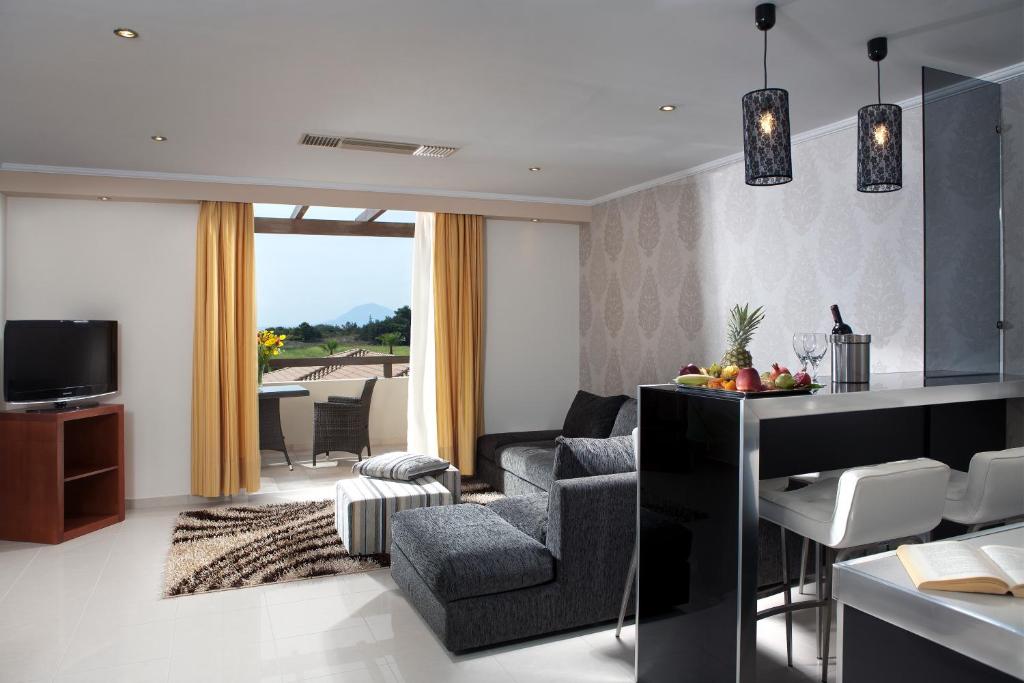 Moderns viesnīcas numurs ar elegantu dizainu, ietverot komfortablu dīvānu un ēdamgaldu ar augļiem. Logi ar skatu uz dārzu un saulainu terasi.