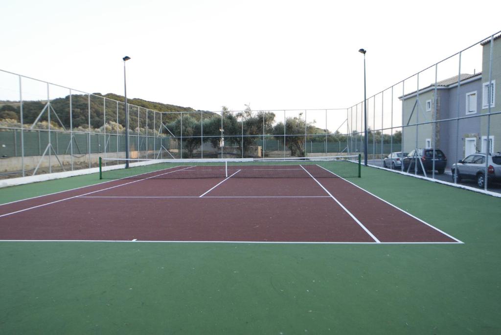Tennis courts with a maroon playing surface and green borders, surrounded by a fence and located near buildings and trees. Perfect for sports enthusiasts.