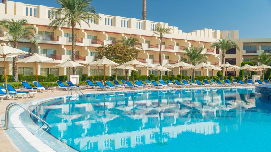 Xperience Kiroseiz Parkland viesnīcas baseins ar sauļošanās krēsliem un palmu kokiem.