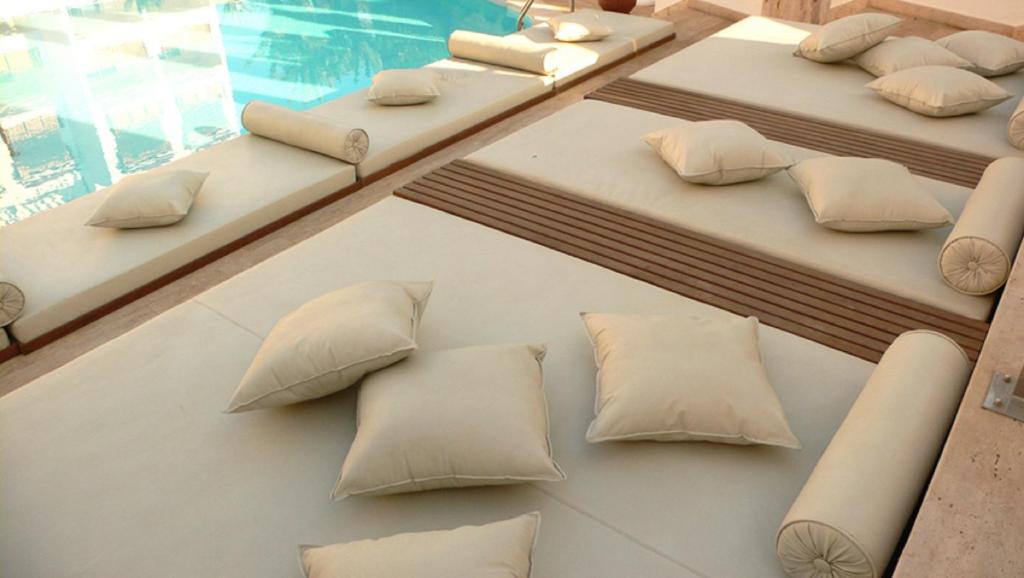 Mīkstas dīvāna spilvenu zonas pie baseina, kas aicina uz relaksāciju un atpūtu. Ideāla vieta brīvā laika pavadīšanai saulainā dienā.