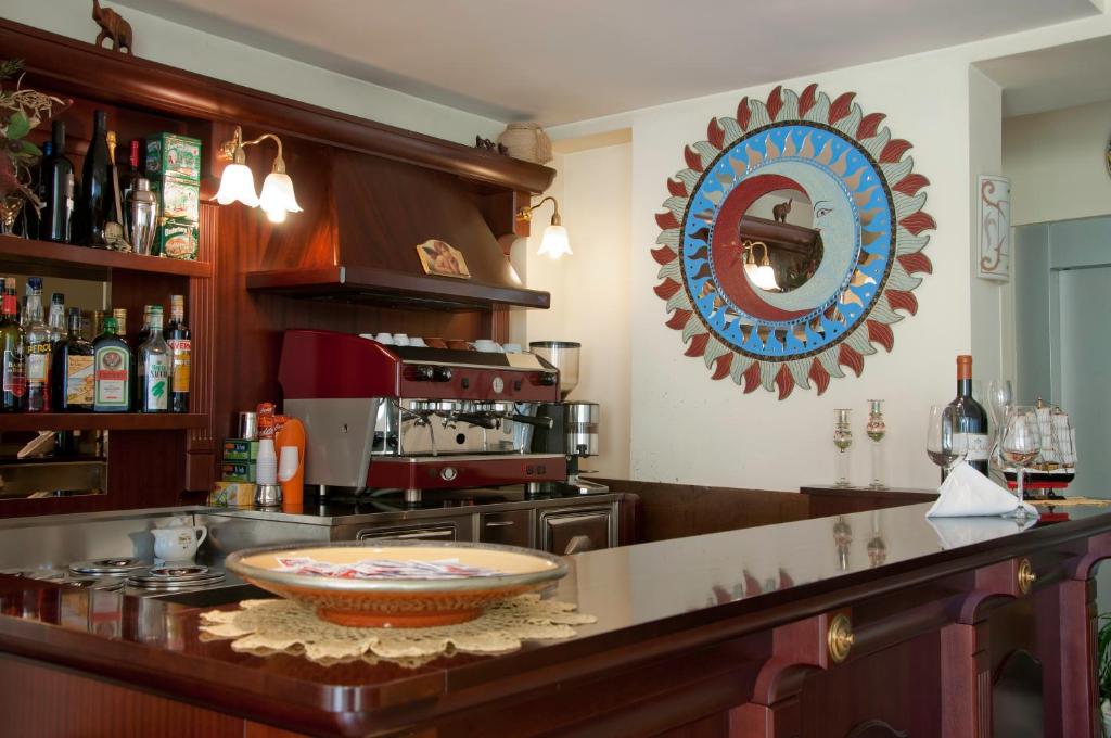 Mūsdienīgs bārs ar elegantu interjeru, kurā ir redzama koka bāra virsma, dzērienu plaukti un kafejnīcas aprīkojums. Uz sienas ir krāsains spogulis, kas piešķir īpašu šarmu.