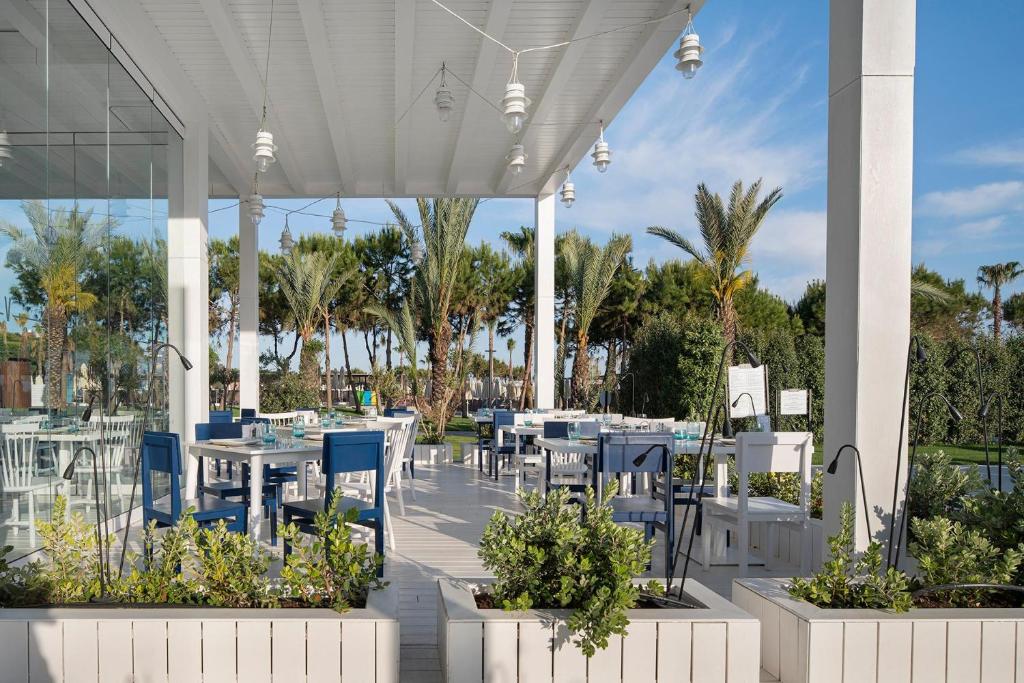 Terases zona ar baltiem galdiem un palmām pie Voyage Belek Golf & Spa.