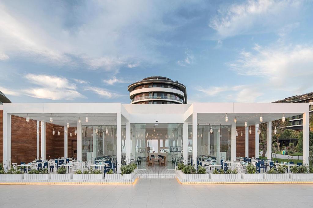 Moderns restorāns pie Voyage Belek Golf & Spa ar stikla fasādi un dārza elementiem.