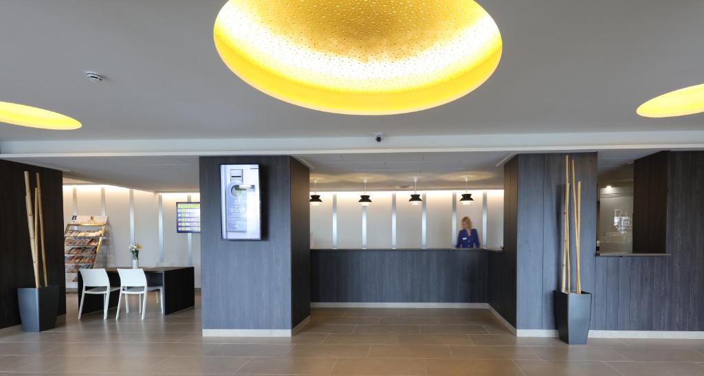 Mūsdienīgs viesnīcas reģistratūras interjers ar elegantu apgaismojumu un uzņemšanas letes dizainu. Redzami arī sēdvietas un dekoratīvi elementi.