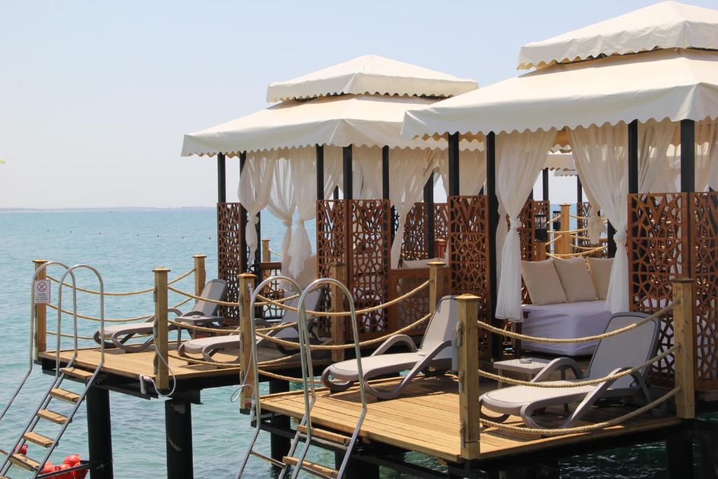 Peldēšanas zona ar elegantiem nojumeņiem un sauļošanās krēsliem virs ūdens, radot relaksējošu atmosfēru. Ideāla vieta atpūtai un saules baudīšanai.