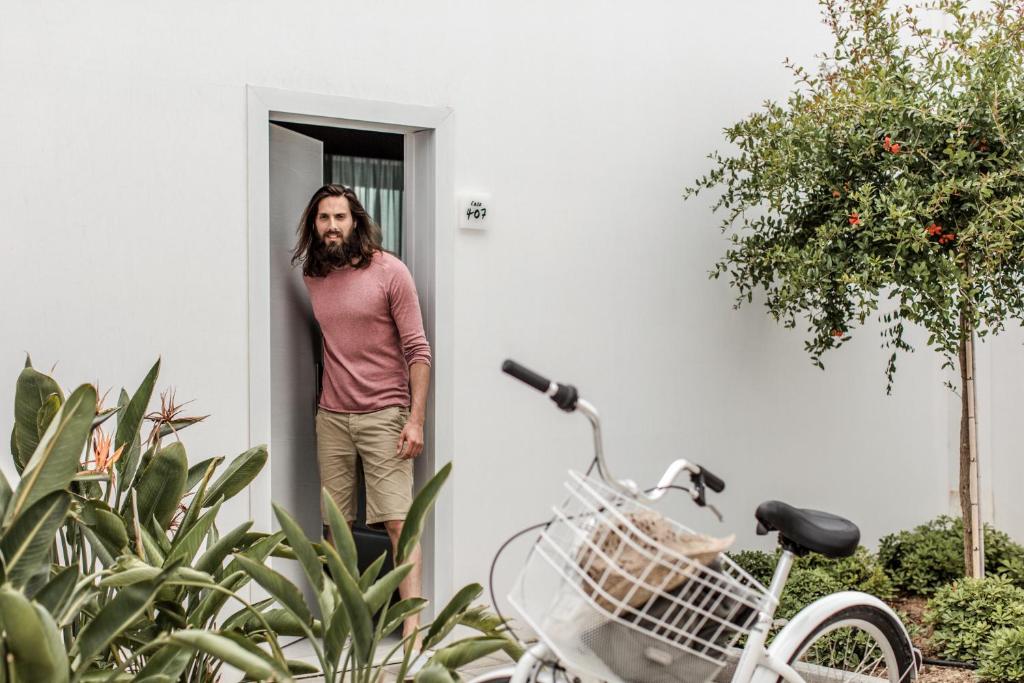 Vīrietis stāv pie durvīm pie Casa Cook Rhodes numura, ar velosipēdu tuvumā.