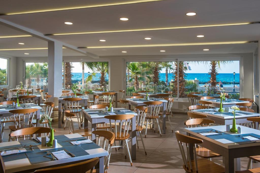 Mūsdienīgs restorāns ar plašiem logiem, caur kuriem redzams jūras skats un palmas. Galdi ir sakārtoti ar ziediem un galdautiem, radot patīkamu un relaksējošu atmosfēru.