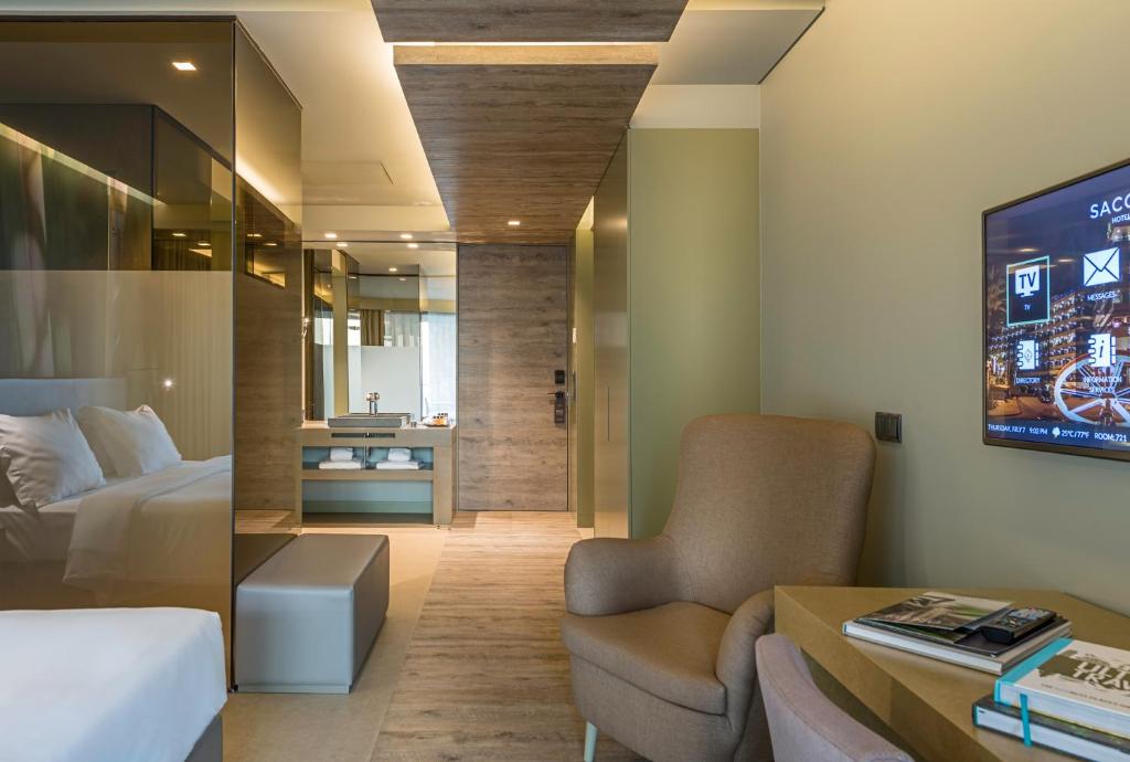 Mūsdienīga viesnīcas istaba ar elegantu interjeru, kurā ir ērta atpūtas zona un moderns televizors. Telpa ir gaiša un plaša, ar stikla sienām un koka apdari.