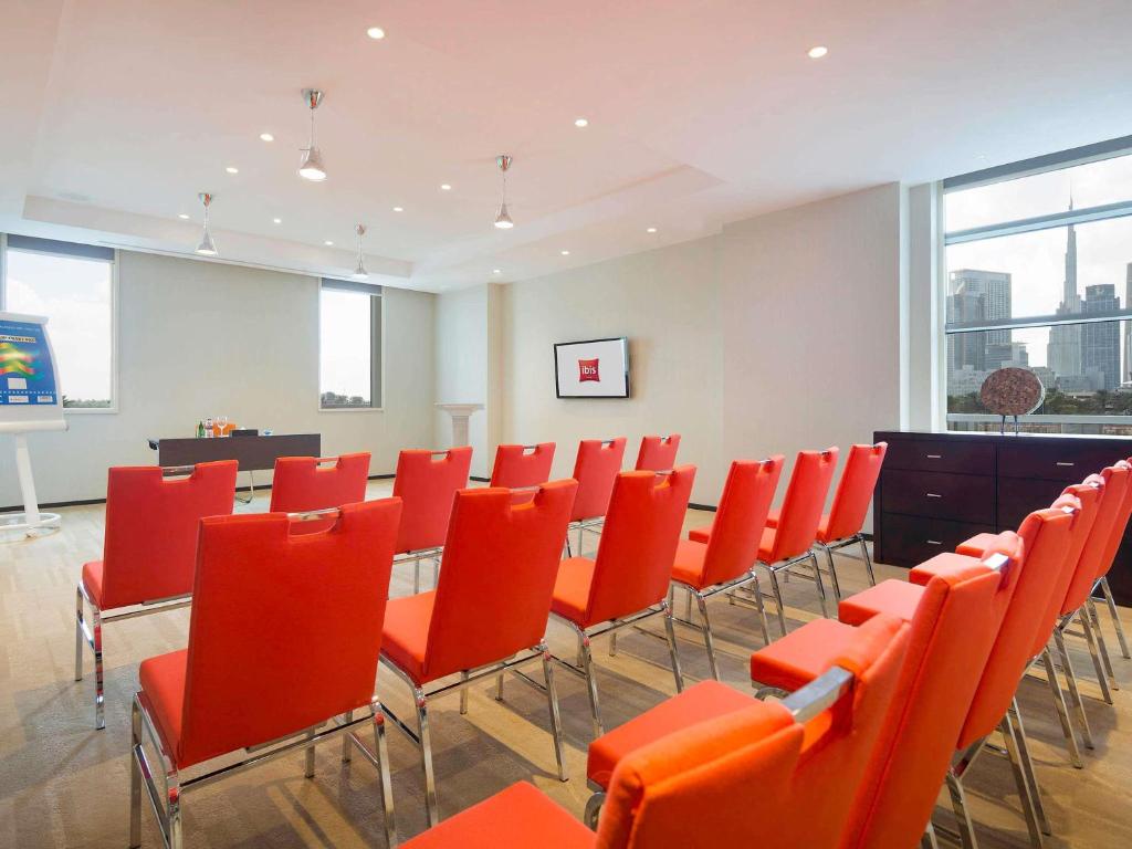 Konferenču zāle Ibis One Central Trade Center viesnīcā ar sarkaniem krēsliem.