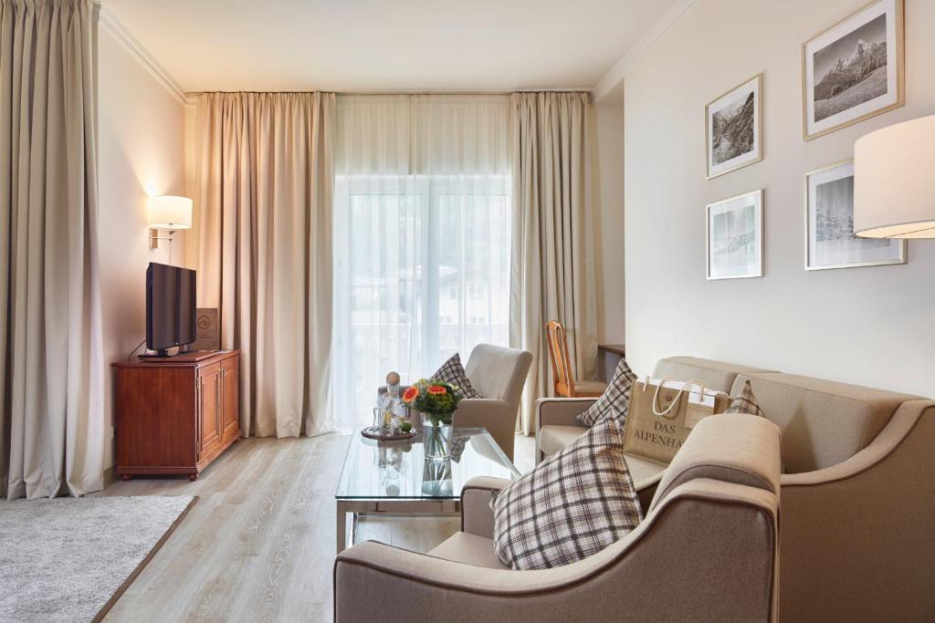 Mūsdienīga viesistaba ar gaišām krāsām, elegantiem dīvāniem un koka televizora galdu. Logu priekšā ir caurspīdīgi aizkari, radot mājīgu atmosfēru.