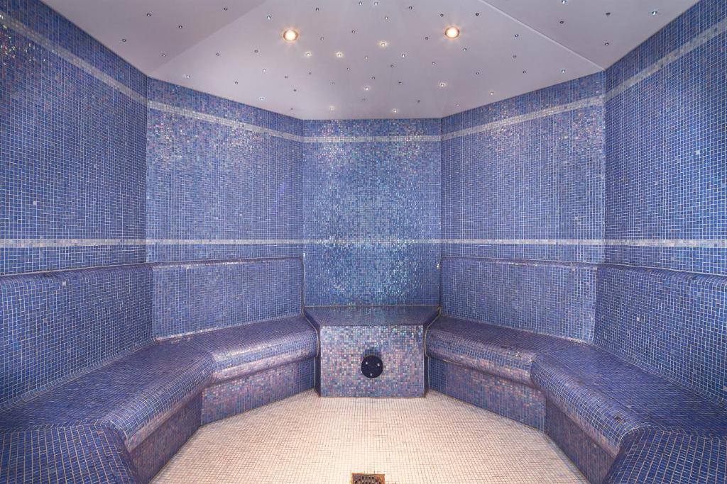 Mūsdienīga tvaika pirts ar zilu mozaīku interjeru un ērtām sēdvietām, radot relaksējošu atmosfēru.