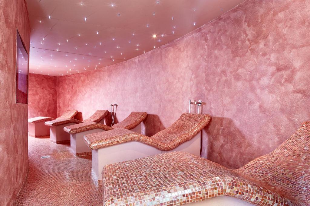 Relaksējoša spa telpa ar rozā sienām un apgaismojumu, kas rada mierīgu atmosfēru, kurā ir komfortabli atpūtas krēsli.