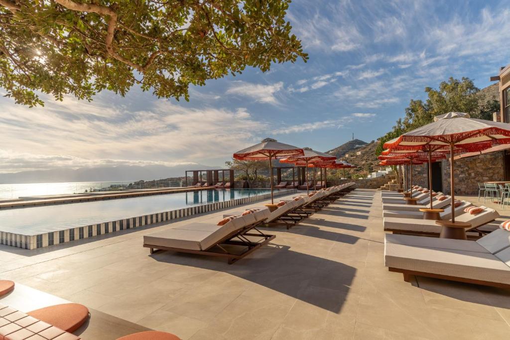 INNSiDE by Meliá Elounda āra baseina zona ar sauļošanās krēsliem un skatu uz jūru un kalniem.