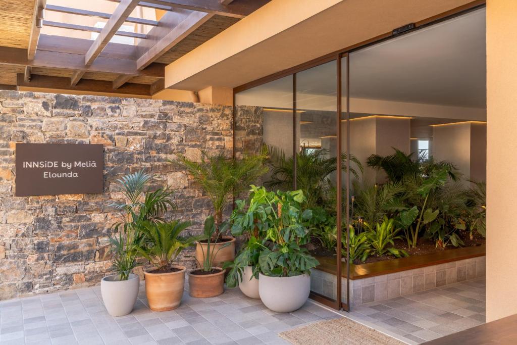 INNSiDE by Meliá Elounda galvenā ieeja ar akmens sienu un zaļiem augiem podos.