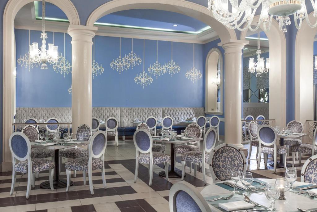 Elegants restorāna interjers ar gaiši zilām sienām un dekoratīvām lustām. Galdi ar stilīgām krēsliem un eleganti klāti galdi.