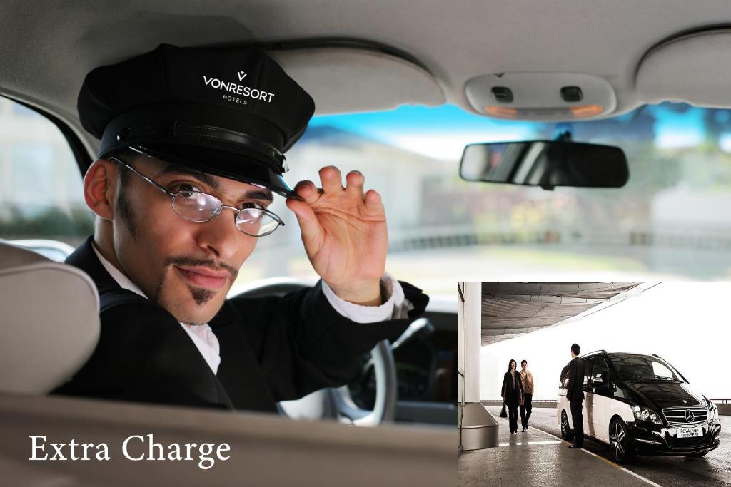 Automašīnas šoferis viesnīcas uniformā sveicina pasažierus, piedāvājot papildu pakalpojumus. Attēlā redzama luksus automašīna un viesi, kas tuvojas.