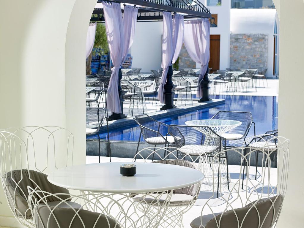 Mūsdienīgs āra kafijas galds ar koka krēsliem pie peldbaseina, ar baltiem un pelēkiem aksesuāriem. Fons ar elegantiem tekstila elementiem un atvērtu telpu.