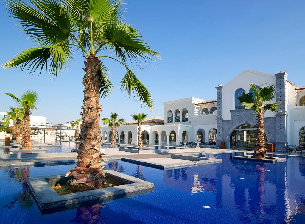 Vasaras kūrorts ar skaidru zilu baseinu, palmām un elegantām arhitektūras detaļām, radot relaksējošu atmosfēru.