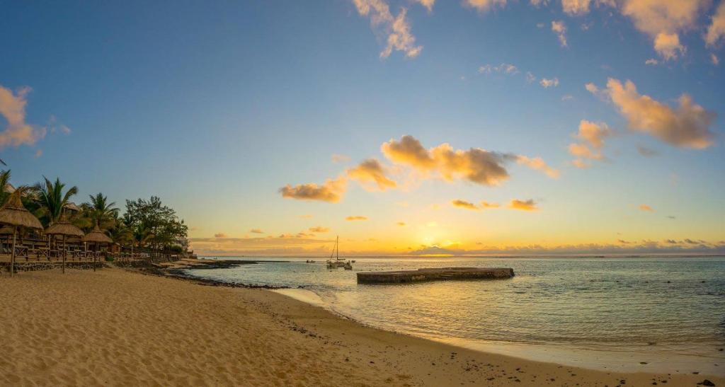 Pūļu pludmales ainava ar saulrietu, mierīgu jūru un kokiem, kas apņem pludmali. Ideāla vieta atpūtai un relaksācijai.