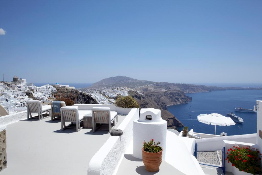 Apskate uz Santorini ar baltām ēkām un jūras ainavu, kurā redzami krēslas krēsli un ziedu pods. Ideāla vieta atpūtai ar skatu uz jūru.