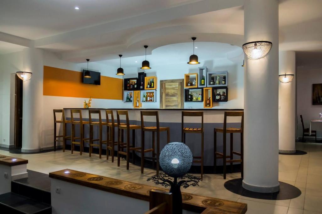 Hotel Plumeria moderns bārs ar augstiem krēsliem un pudelēm plauktos.