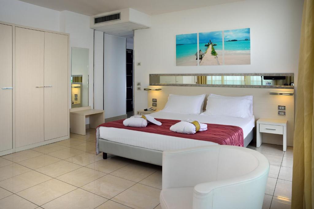 Mūsdienīga viesnīcas numura interjers ar divguļamo gultu, elegantu mēbeļu un gaismas elementiem. Uz sienas ir ainava ar pludmali, radot relaksējošu atmosfēru.