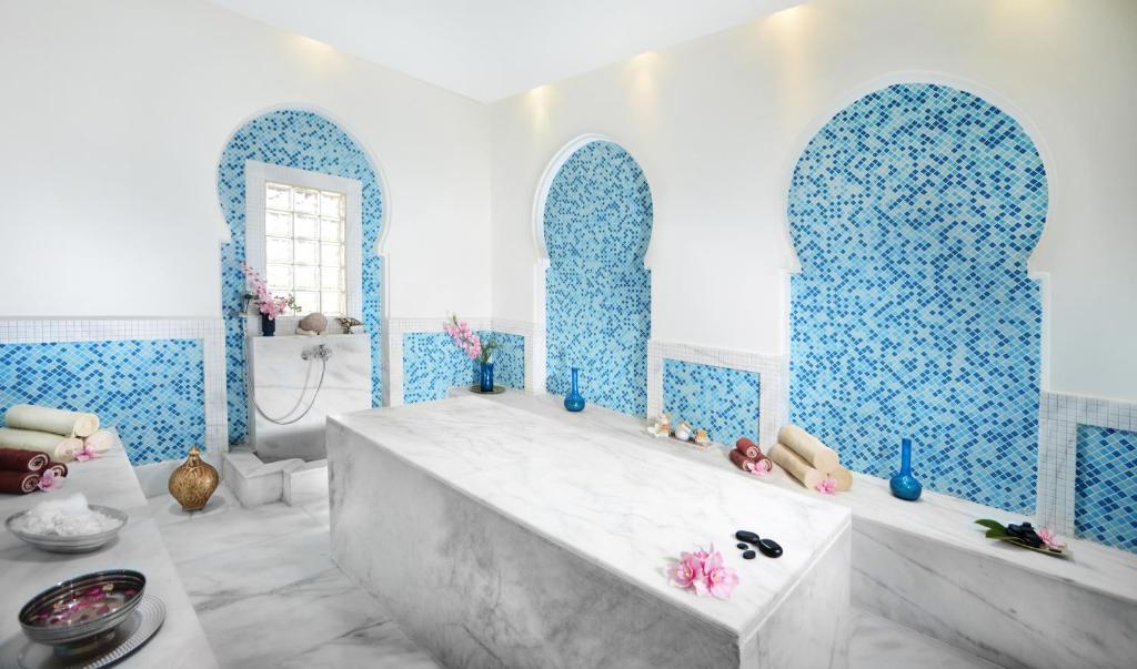 Elegants spa interjers ar ziliem mozaīkas elementiem, marmora galdu un relaksējošām akcesorijām, piemērots atpūtai un labsajūtai.