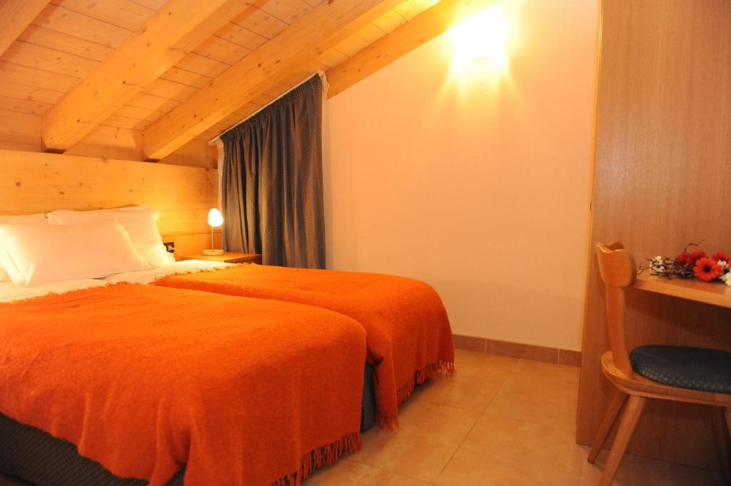 Siltā un mājīgā guļamistaba ar divām gultām, kas pārklātas ar oranžām segām, un koka griestiem, papildināta ar gaismu un nelielu rakstāmgaldu.