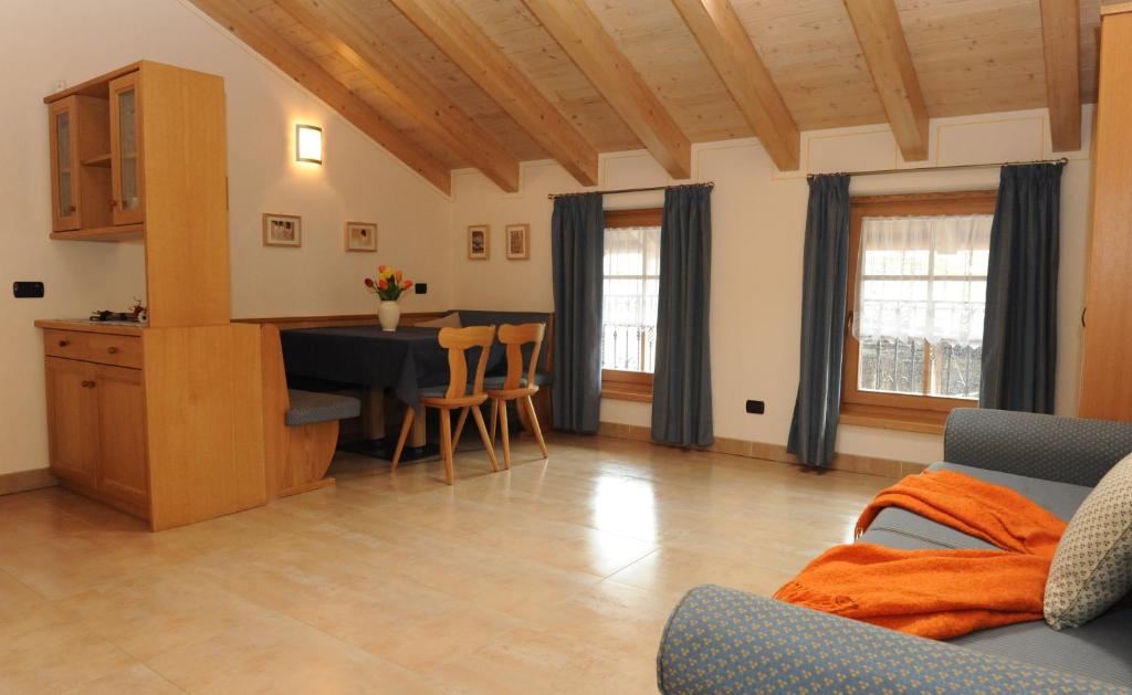 Mūsdienīgs viesistabas interjers ar koka griestiem, ēdamgaldu un dīvānu, kas rotāts ar oranžu segu. Gaisma ieplūst caur logiem ar ziliem aizkariem, radot mājīgu atmosfēru.