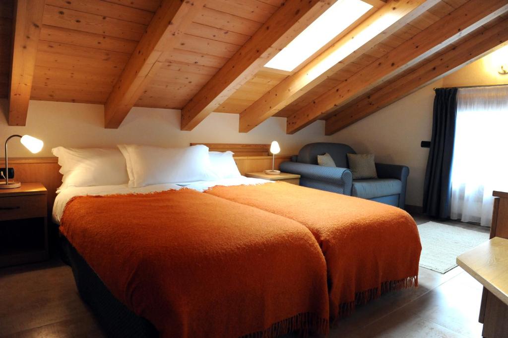 Mūsdienīgs viesnīcas numurs ar divām gultām, kas pārklātas ar oranžām segām, un koka griestiem ar redzamām sijas. Numurā ir dīvāns un galda lampa, radot mājīgu atmosfēru.