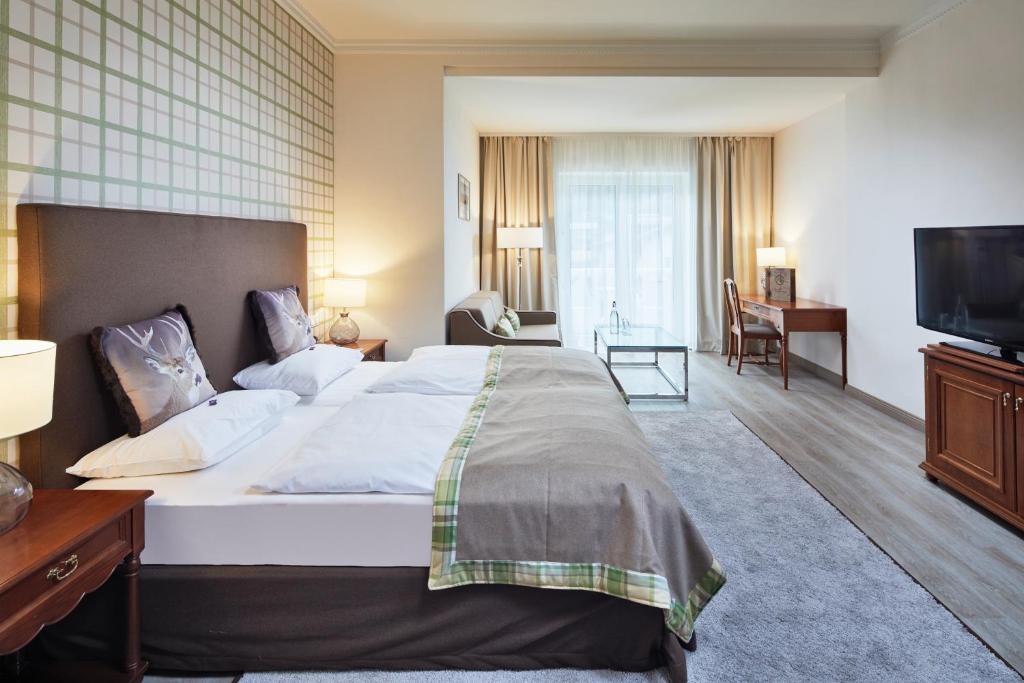 Mūsdienīgs viesnīcas numurs ar divguļamo gultu, koka mēbelēm un lieliem logiem, kas nodrošina dabisko apgaismojumu. Telpai ir silts un viesmīlīgs noskaņojums, ideāli piemērota atpūtai.