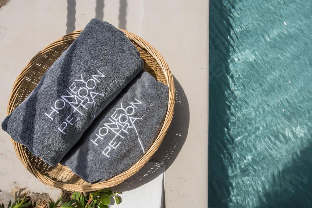 Dvieļi ar "HONEYMOON PETRA" logo, novietoti grozā blakus peldbaseinam, rada relaksējošu atmosfēru.