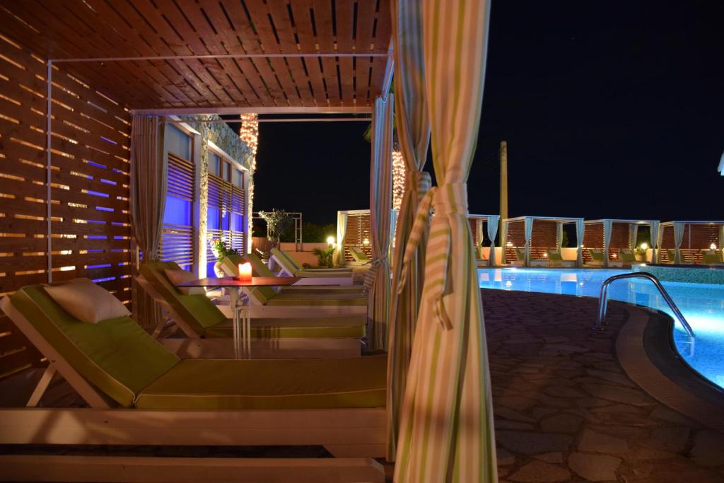 Eleganta atpūtas zona pie baseina ar zaļām sauļošanās krēslām un romantisku apgaismojumu naktī. Redzama baseina mala un kabīnes, kas piedāvā privātumu un relaksāciju.