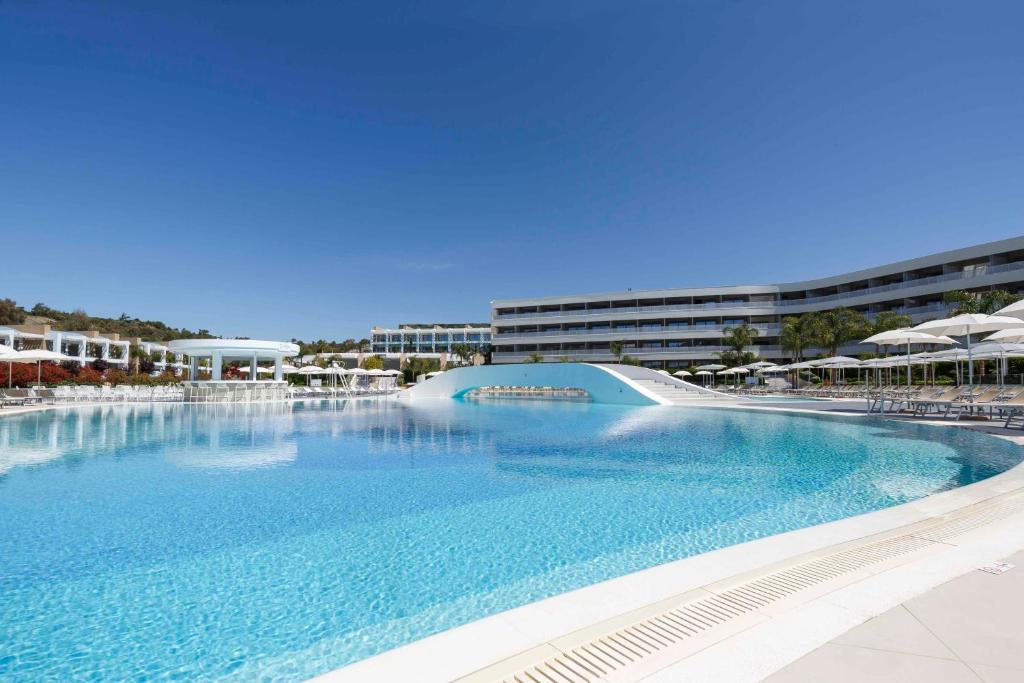 Peldbaseins pie Princess Andriana Resort & Spa ar modernām ēkām fona.