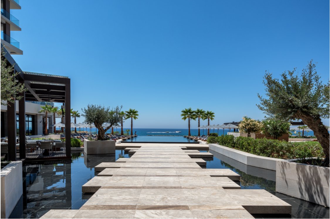 Mūsdienīgs kūrorts ar skatu uz jūru, kur ūdens tilti ved uz atpūtas zonām un palmām saulainā dienā. panoramic view with beach and pools